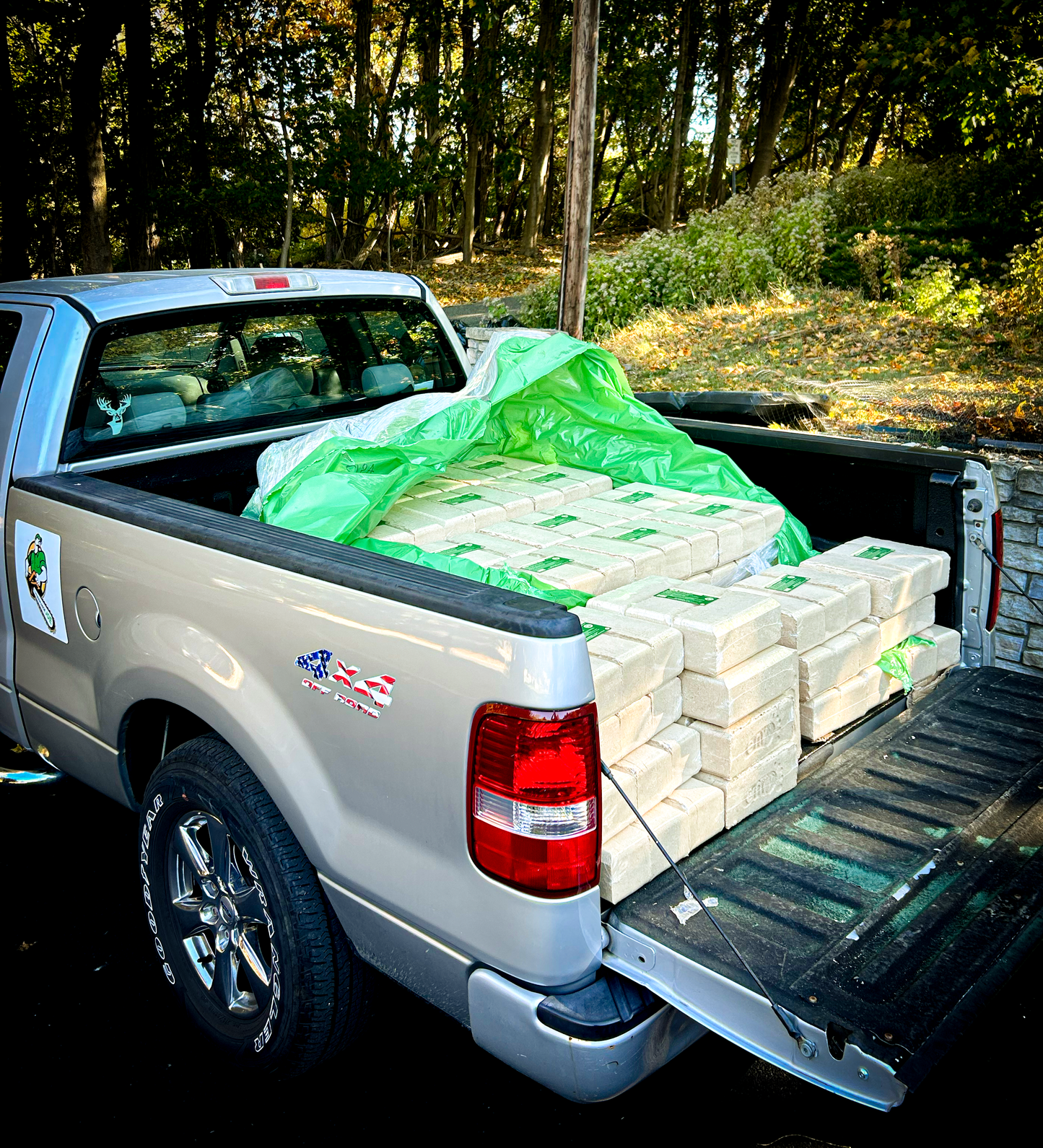 Truck with a bed full of envi blocks and green plastic sheeting in a wooded area.