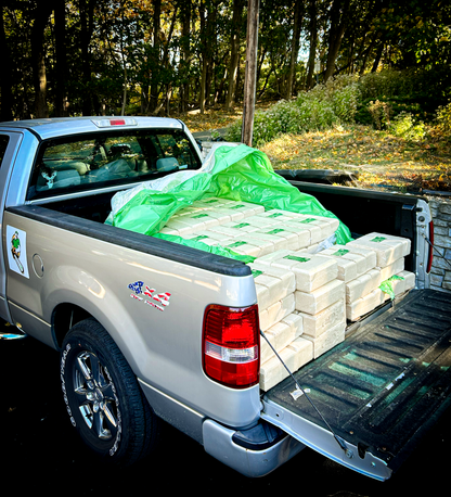 Truck with a bed full of envi blocks and green plastic sheeting in a wooded area.